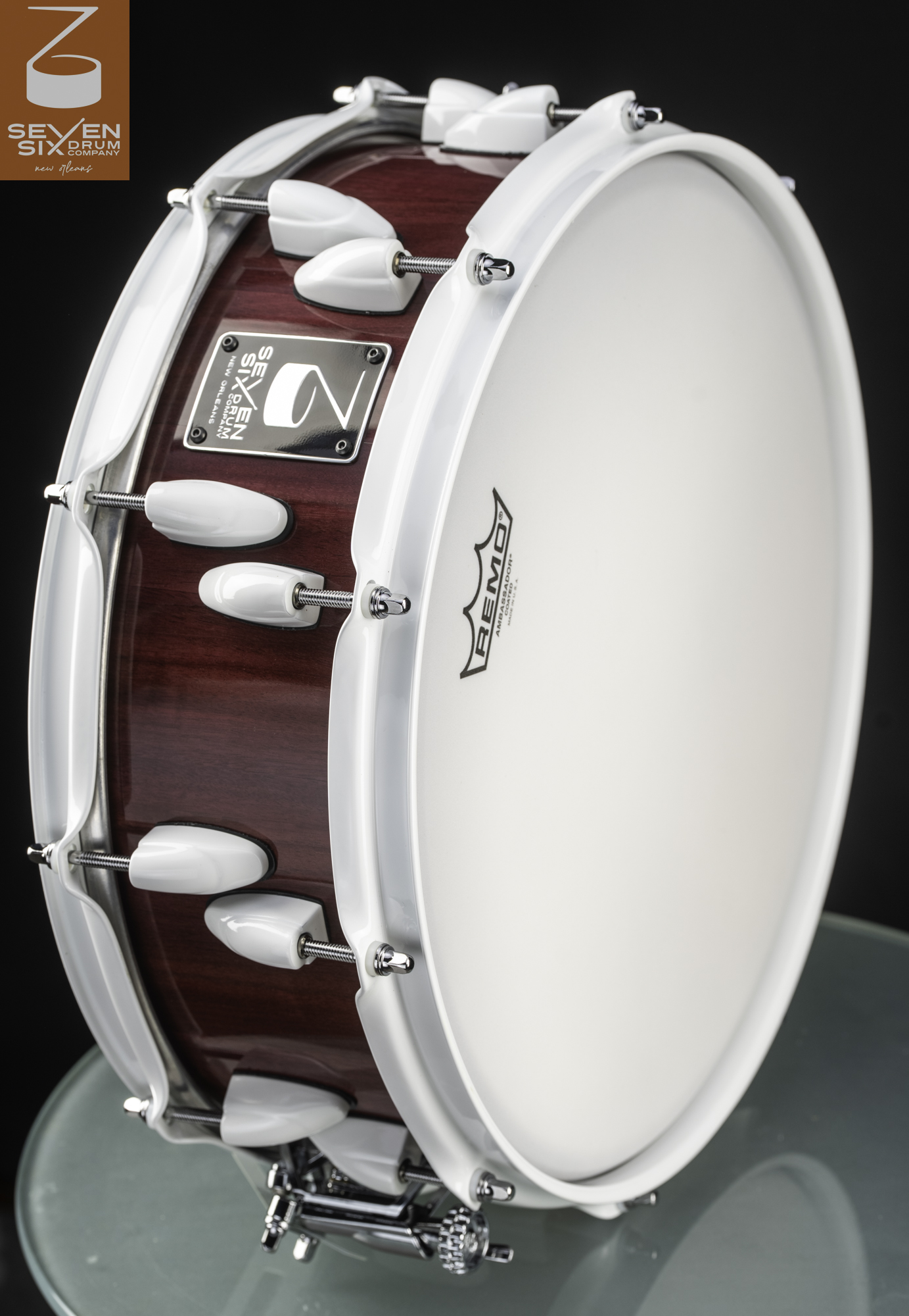 Handmade snare drum featuring a burgundy stained wood shell, glossy white hoops, and matching white lugs.