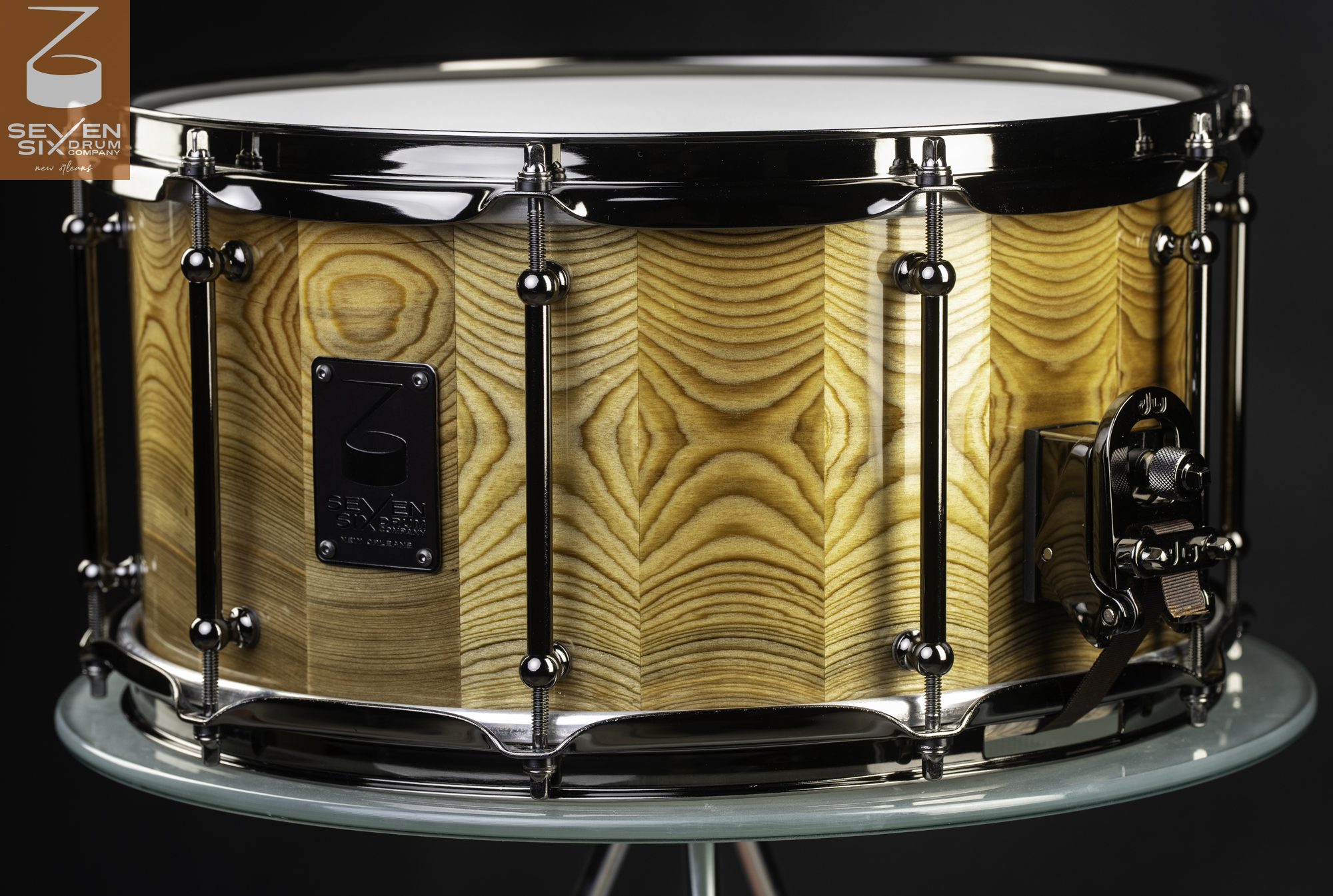 Handmade snare drum with a glossy chevron-grain wood shell, black nickel tube lugs, and matching hoops.