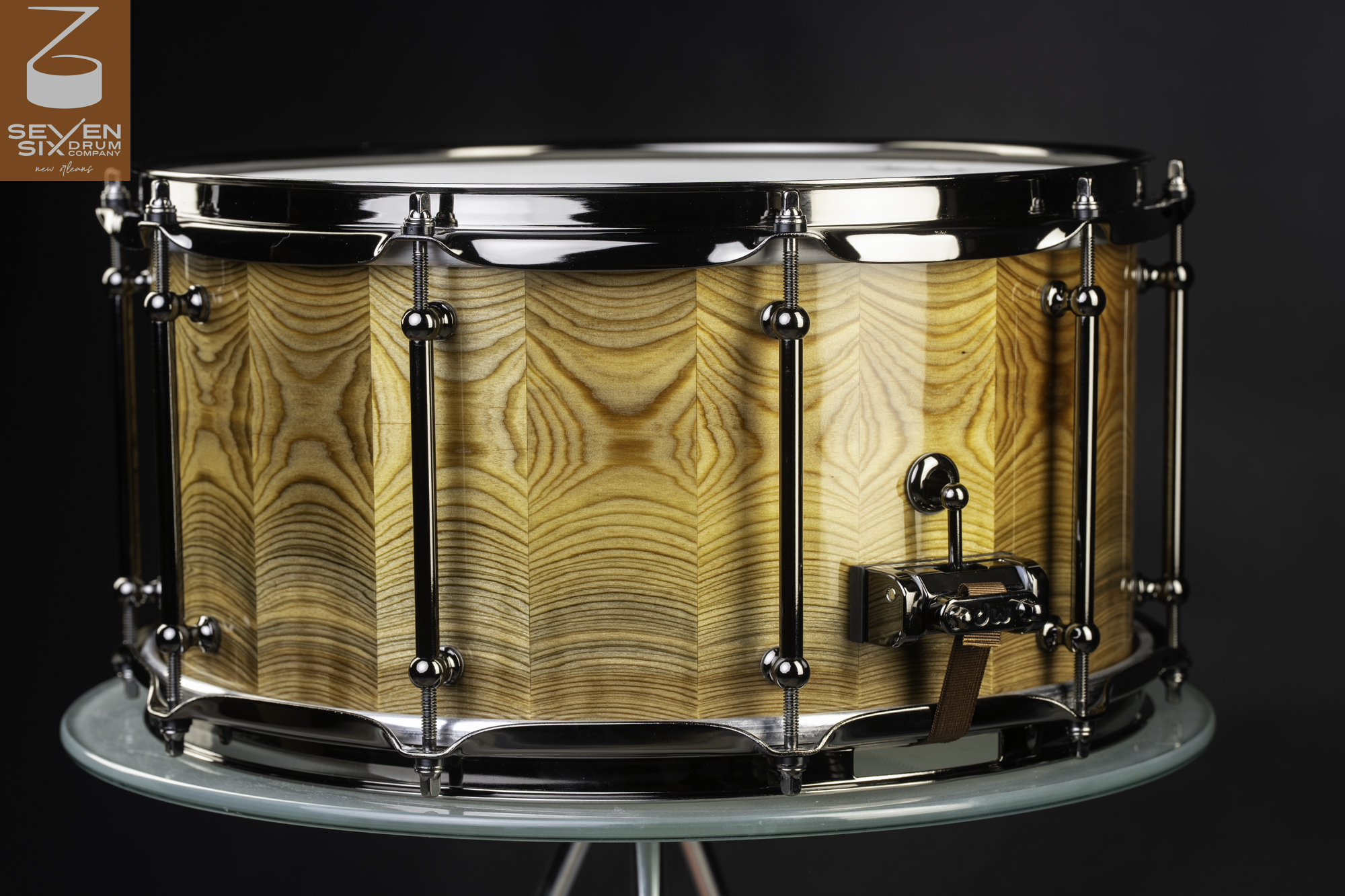 Handmade snare drum featuring a glossy segmented wood shell with black nickel tube lugs and hoops.