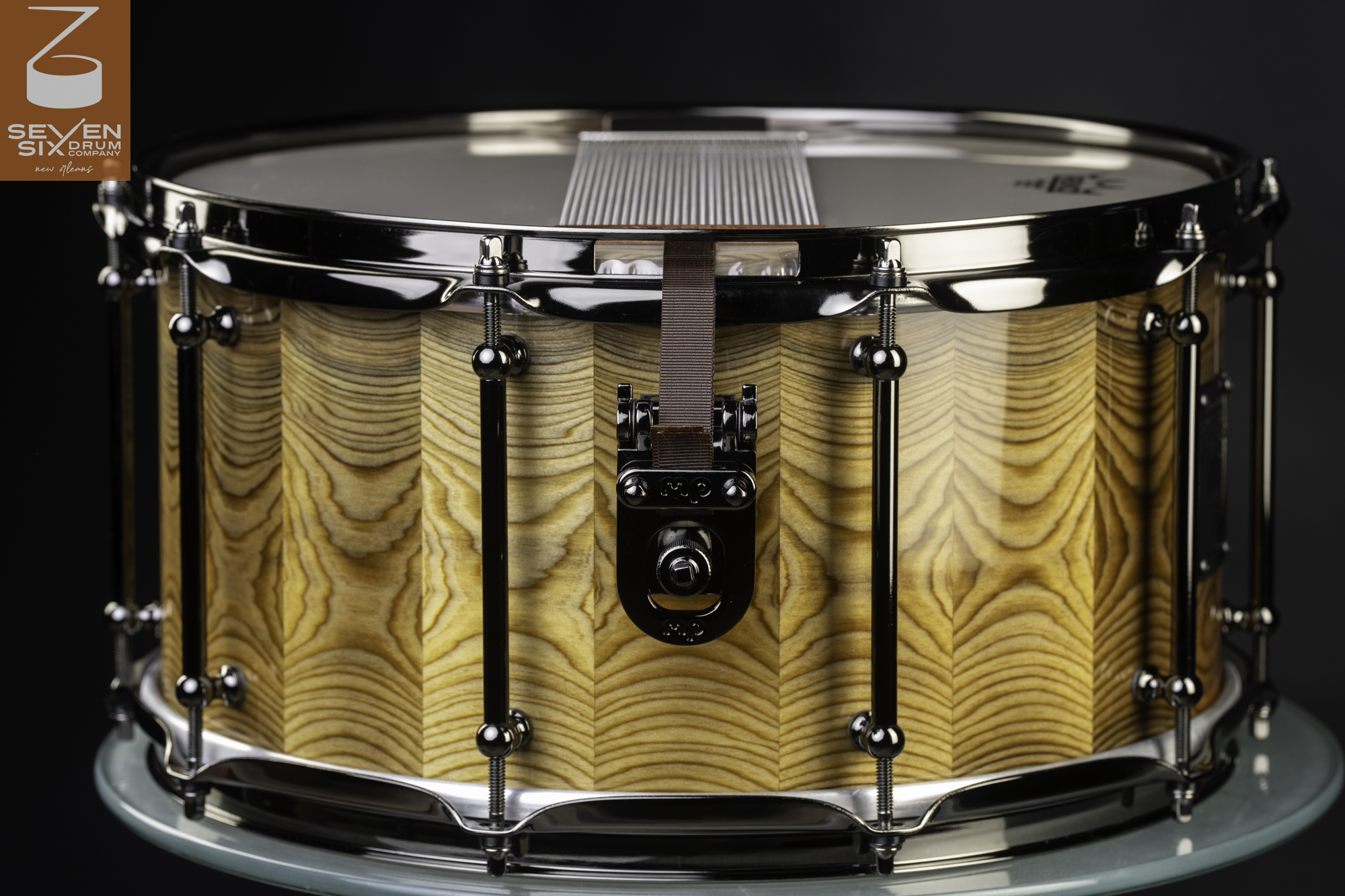 Gloss-finished segmented wood snare drum featuring black nickel tube lugs, hoops, and a snare butt plate.