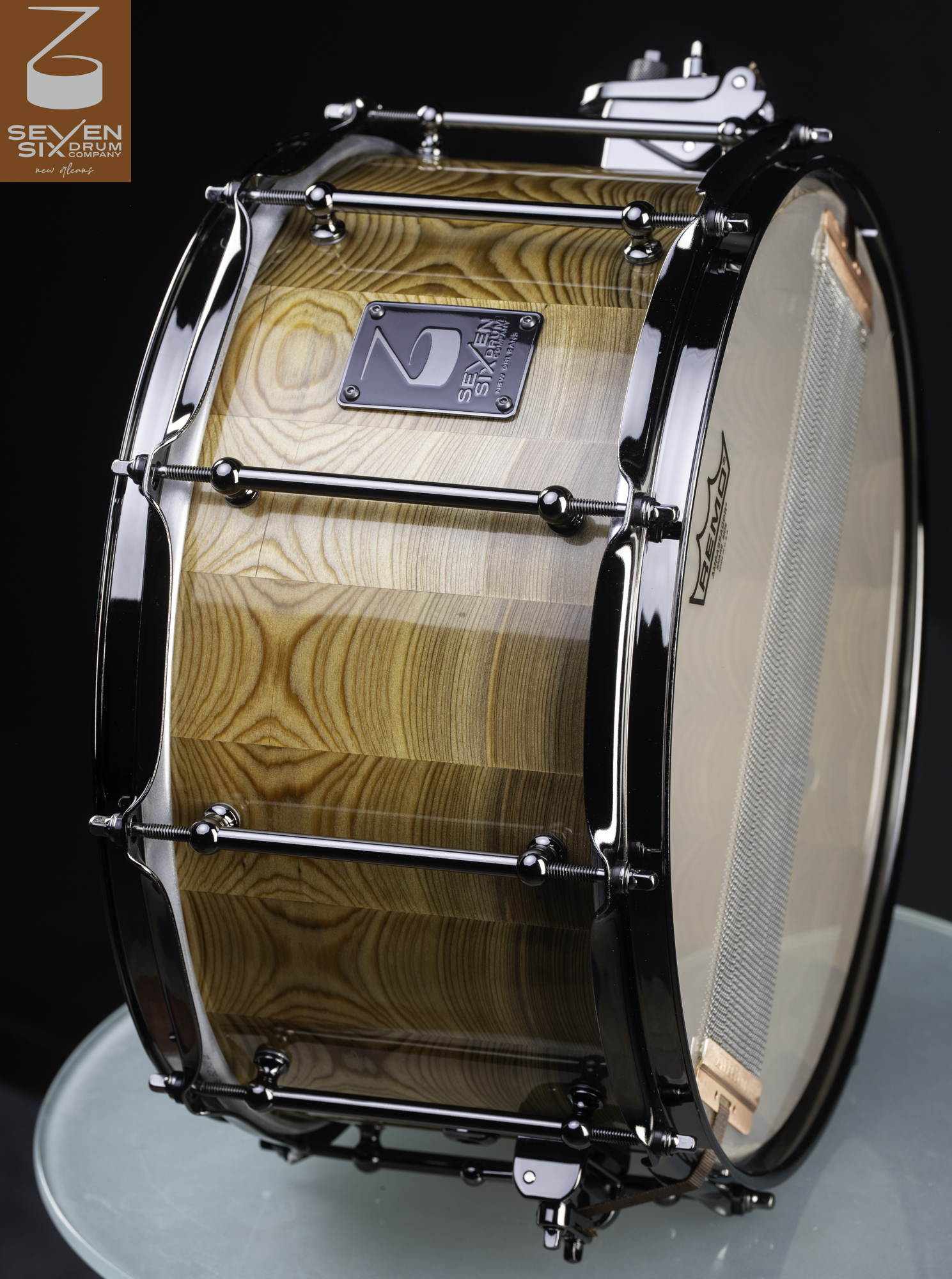 Handmade snare drum featuring a glossy natural wood shell with black nickel tube lugs and hoops.