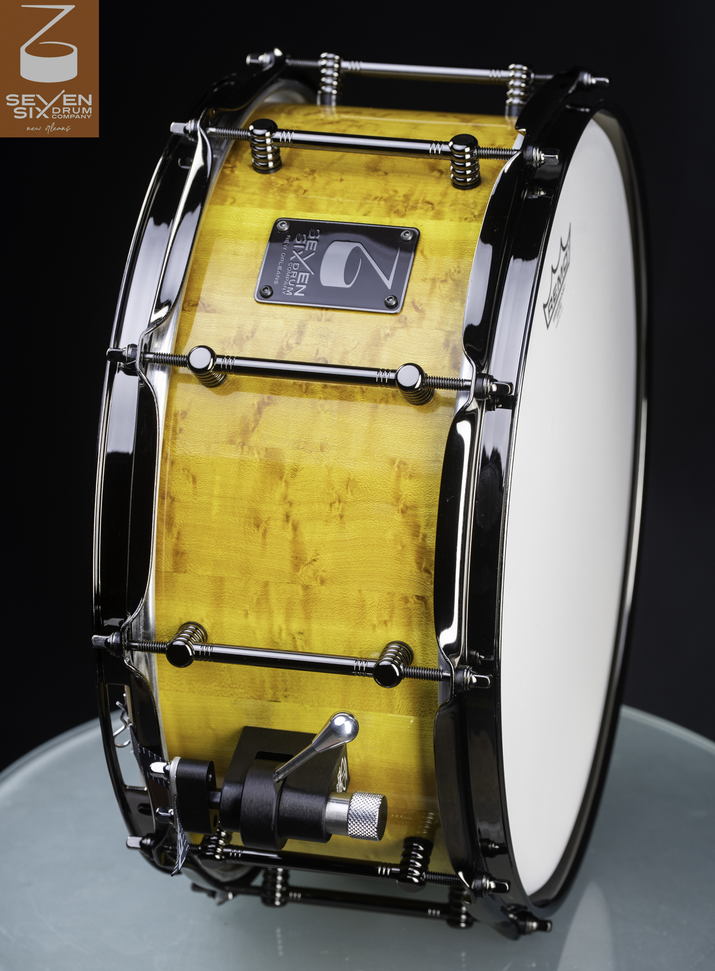 Handmade snare drum with a glossy amber maple shell, black nickel hoops and tube lugs, and a black throw-off.