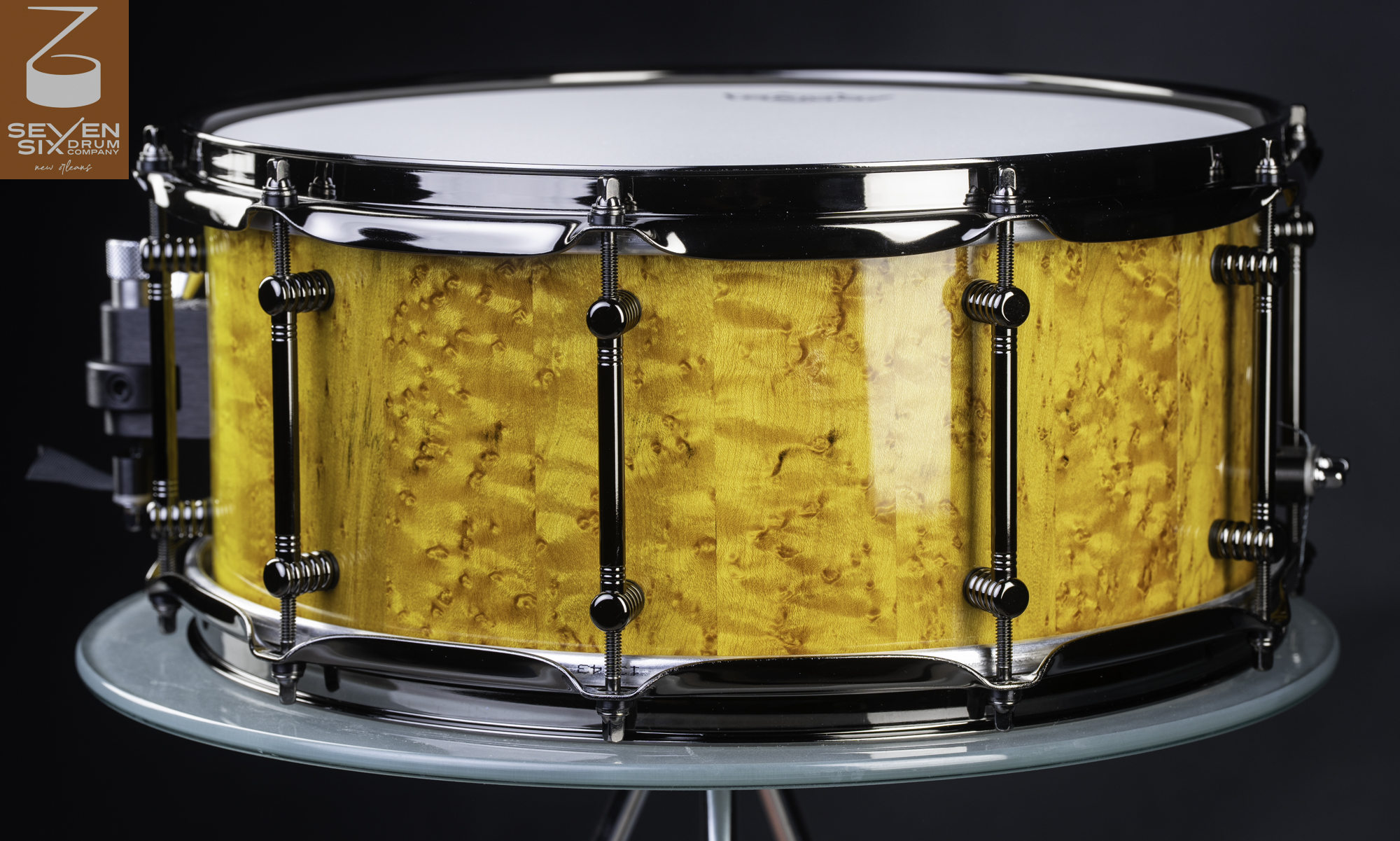 Handmade snare drum with a glossy golden burl wood shell, black nickel tube lugs, and matching hoops.