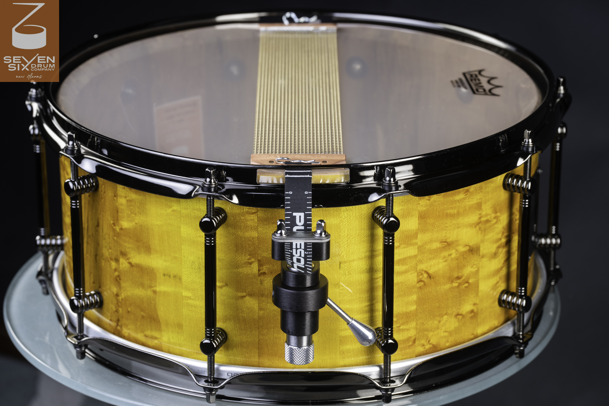 Handmade snare drum with a gloss yellow figured maple shell, black nickel hardware, and snare wires connected to a throw-off.