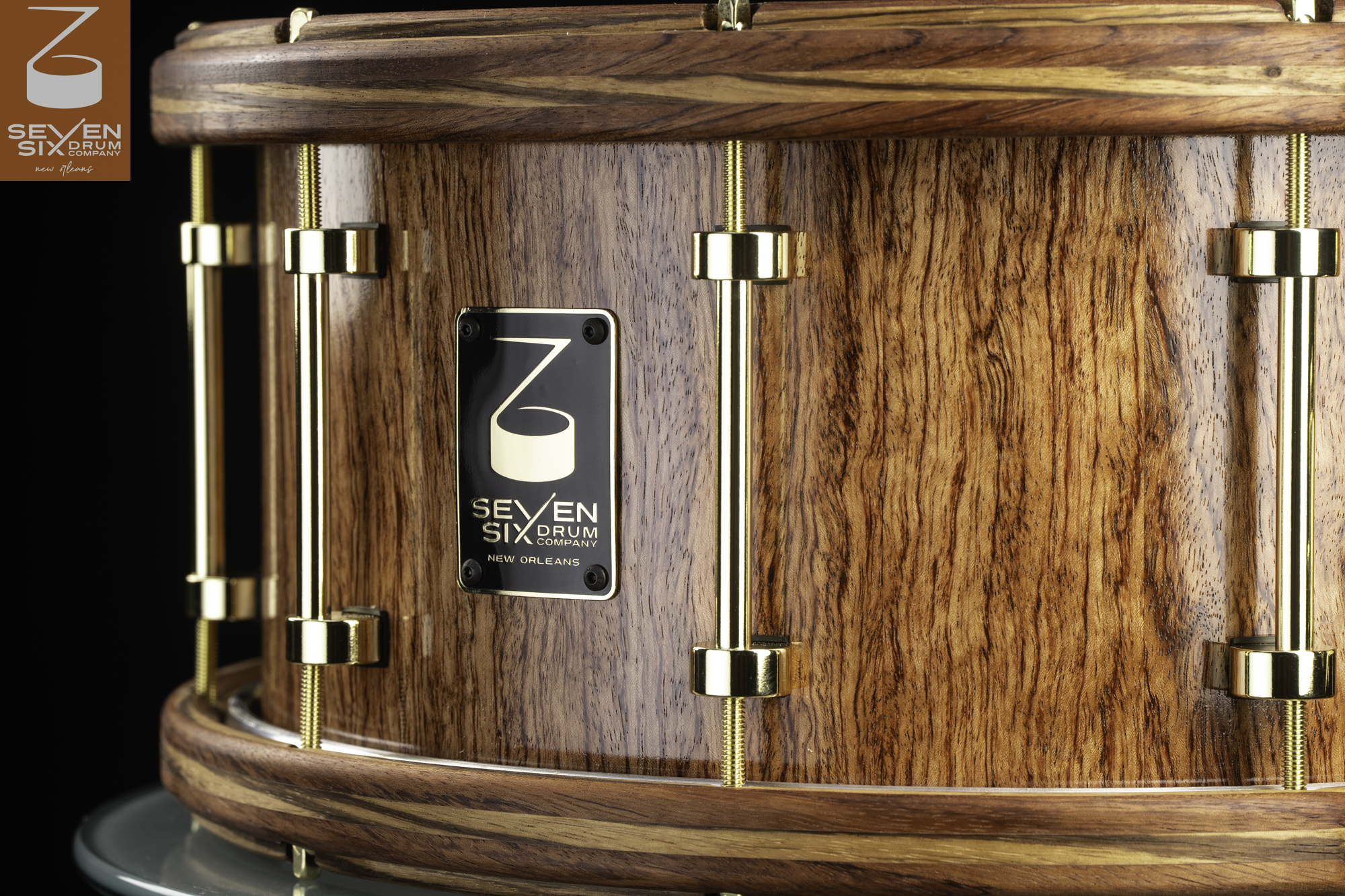 Handcrafted snare drum with a glossy natural wood shell, matching wood hoops, and polished brass tube lugs.