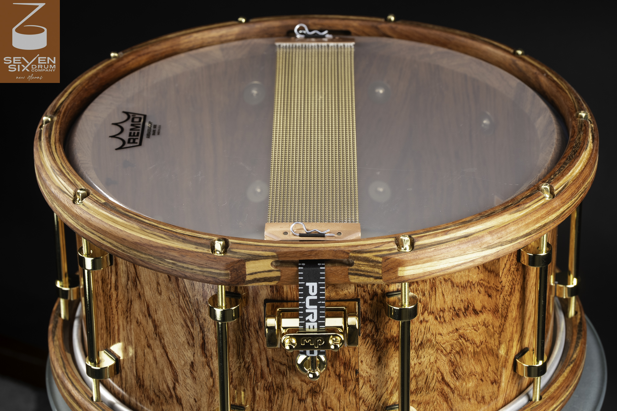 Handmade wood snare drum with a natural finish, matching wood hoops, gold hardware, and brass snare wires.