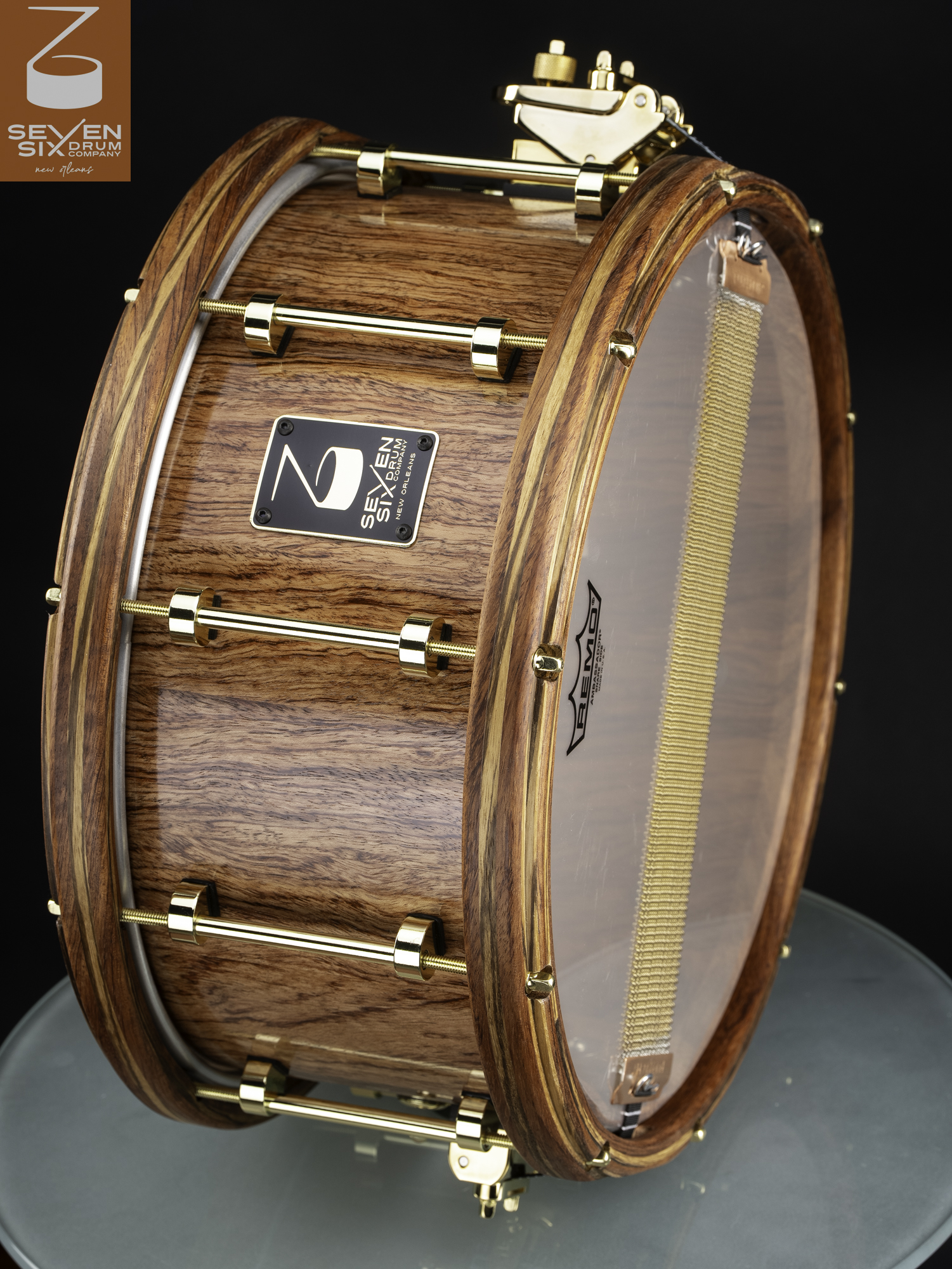 Glossy natural wood snare drum featuring matching wooden hoops, polished gold tube lugs, and a gold throw-off.