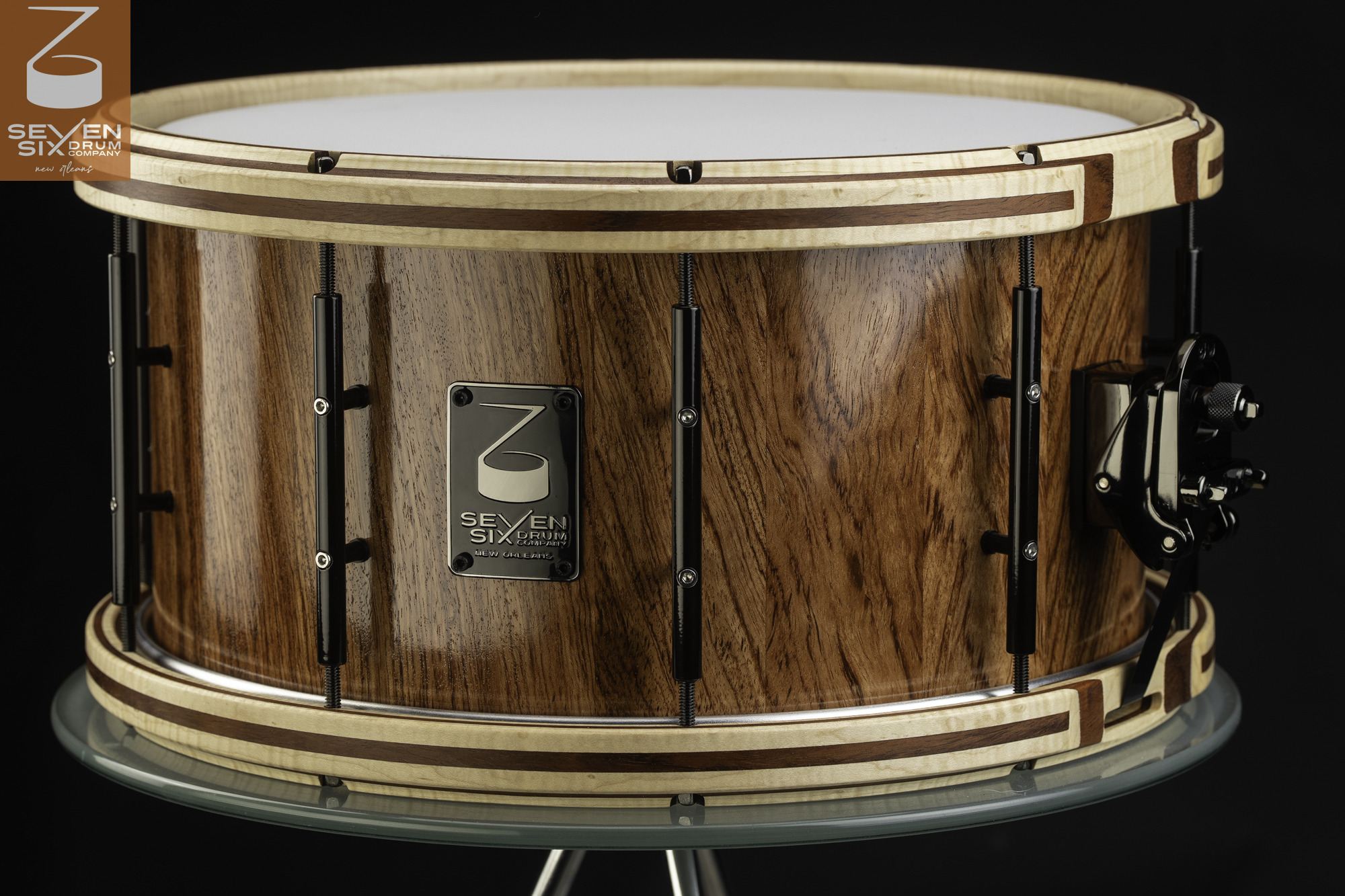 Glossy wood snare drum with inlaid wooden hoops, black tube lugs, and a black snare throw-off.