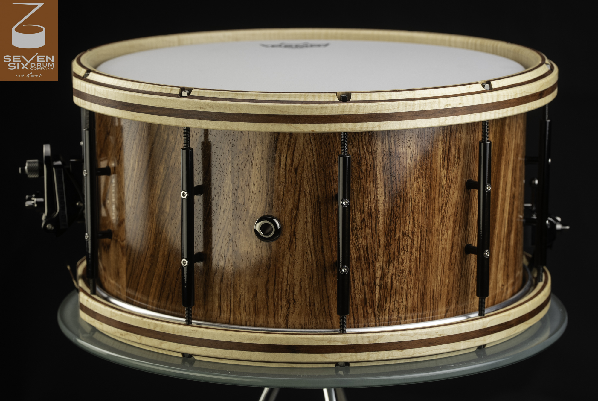 Handmade snare drum with a glossy natural wood shell, striped wooden hoops, and black tube lugs.