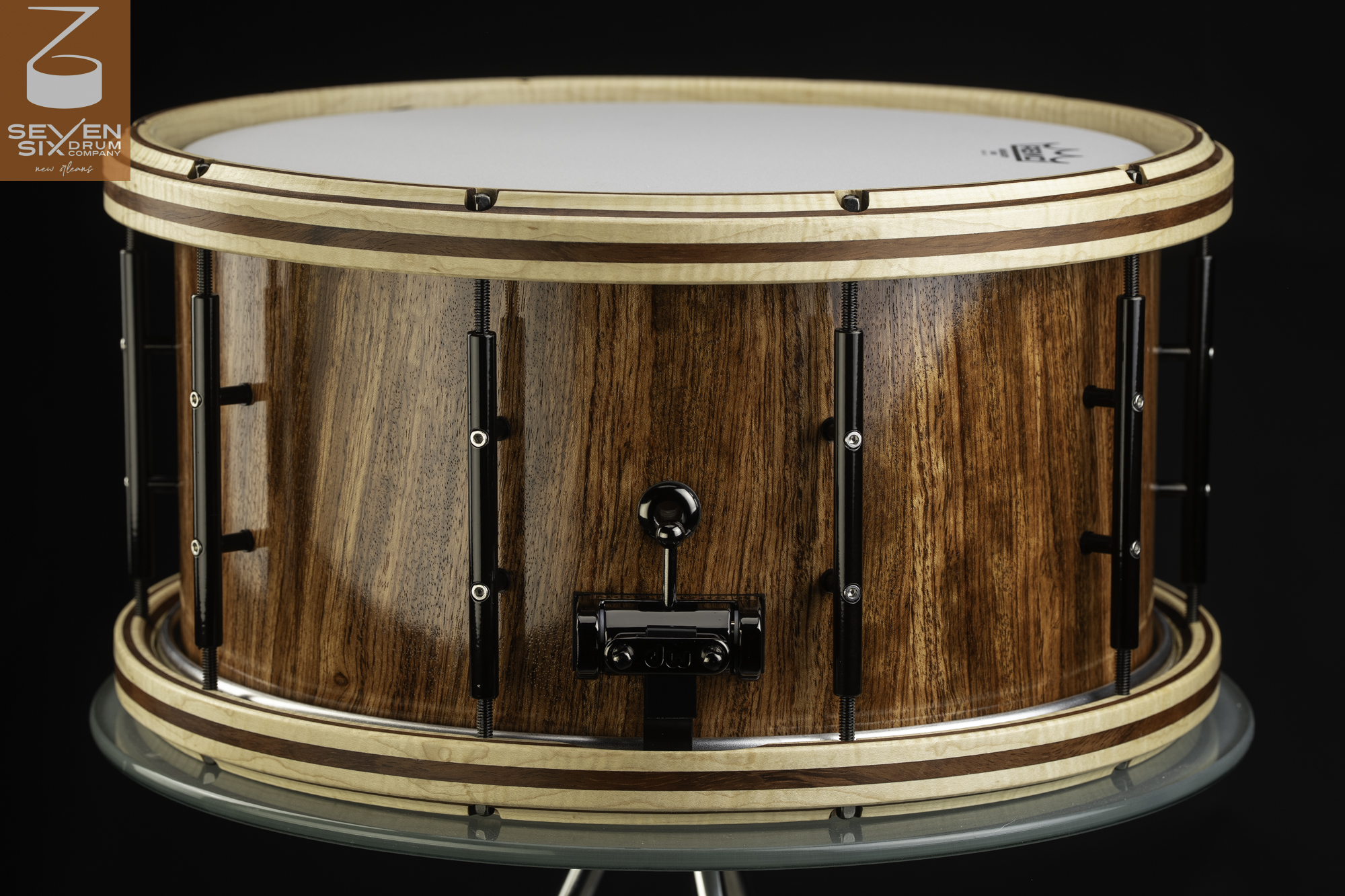 Handmade snare drum featuring a high-gloss wood shell, striped wooden hoops, and black hardware with tube lugs and throw-off.