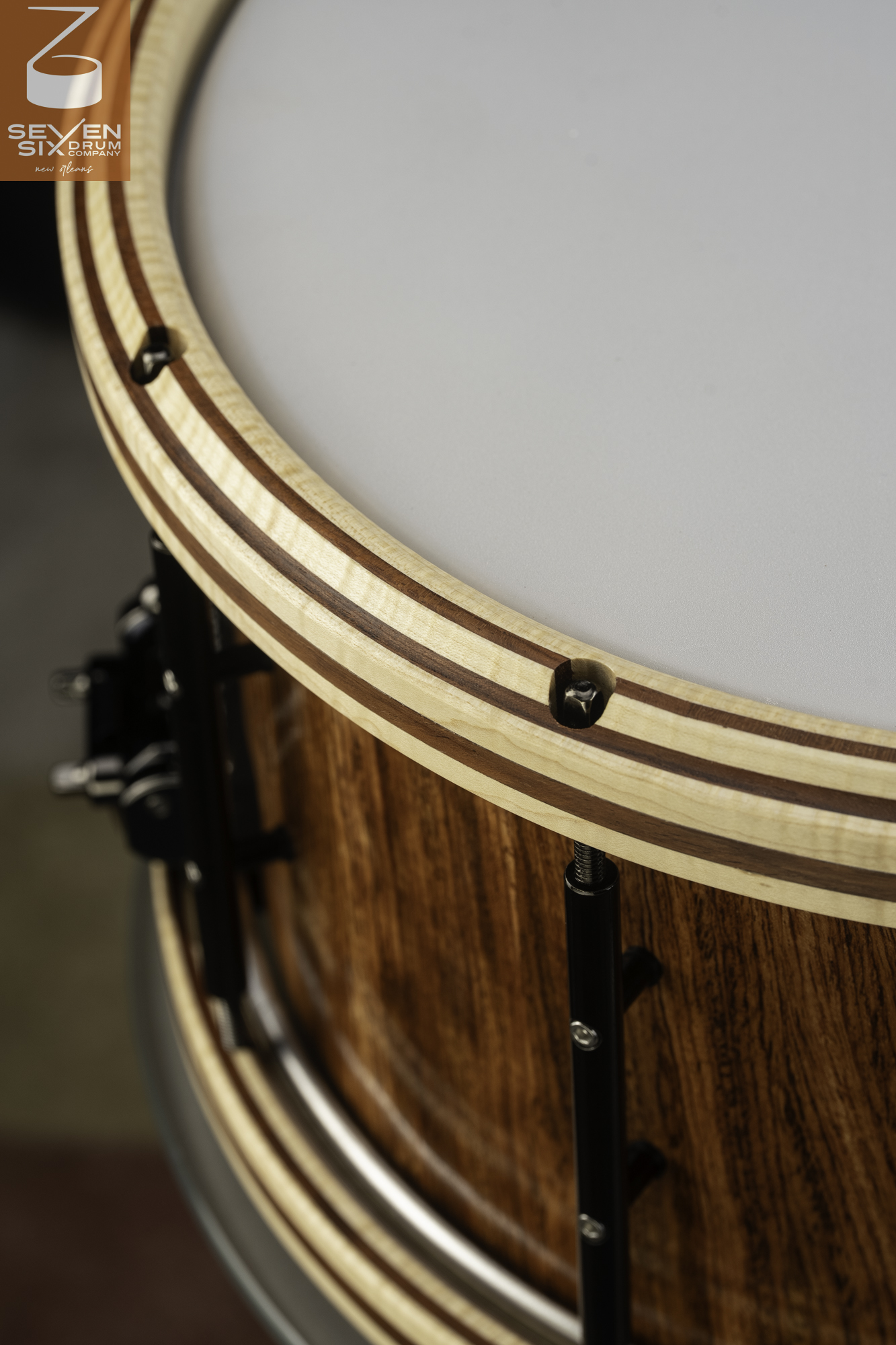 Handcrafted snare drum featuring a gloss wood shell, striped wooden hoop, and black hardware with recessed tension rods.