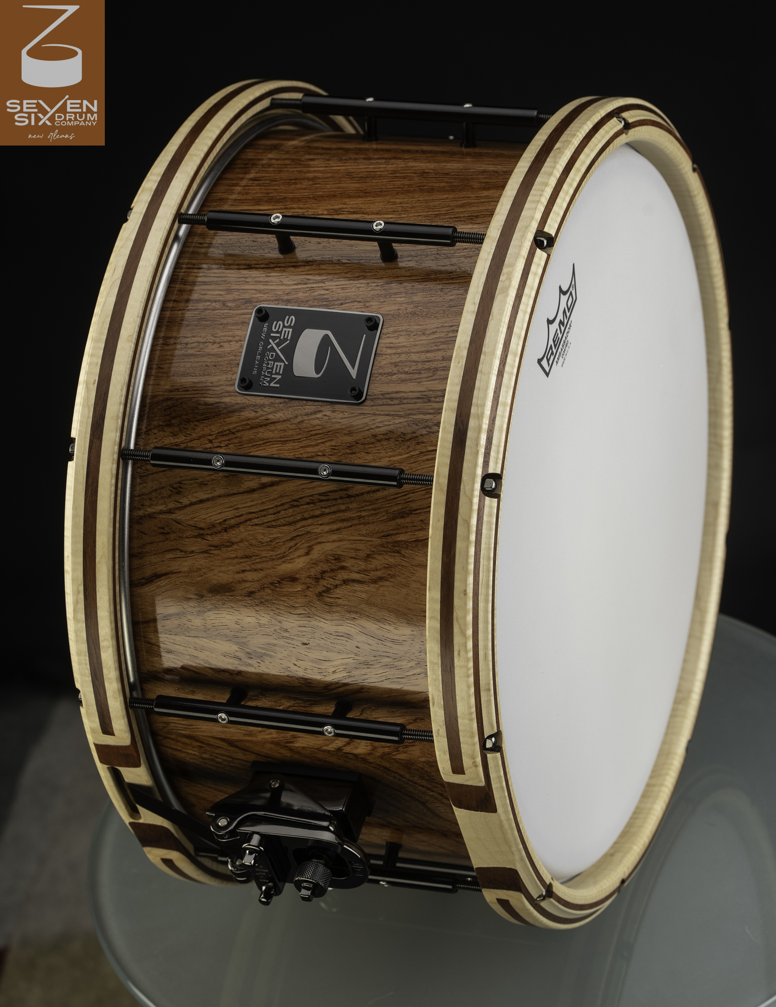Glossy wood snare drum featuring inlaid wooden hoops, black tube lugs, and a black throw-off.