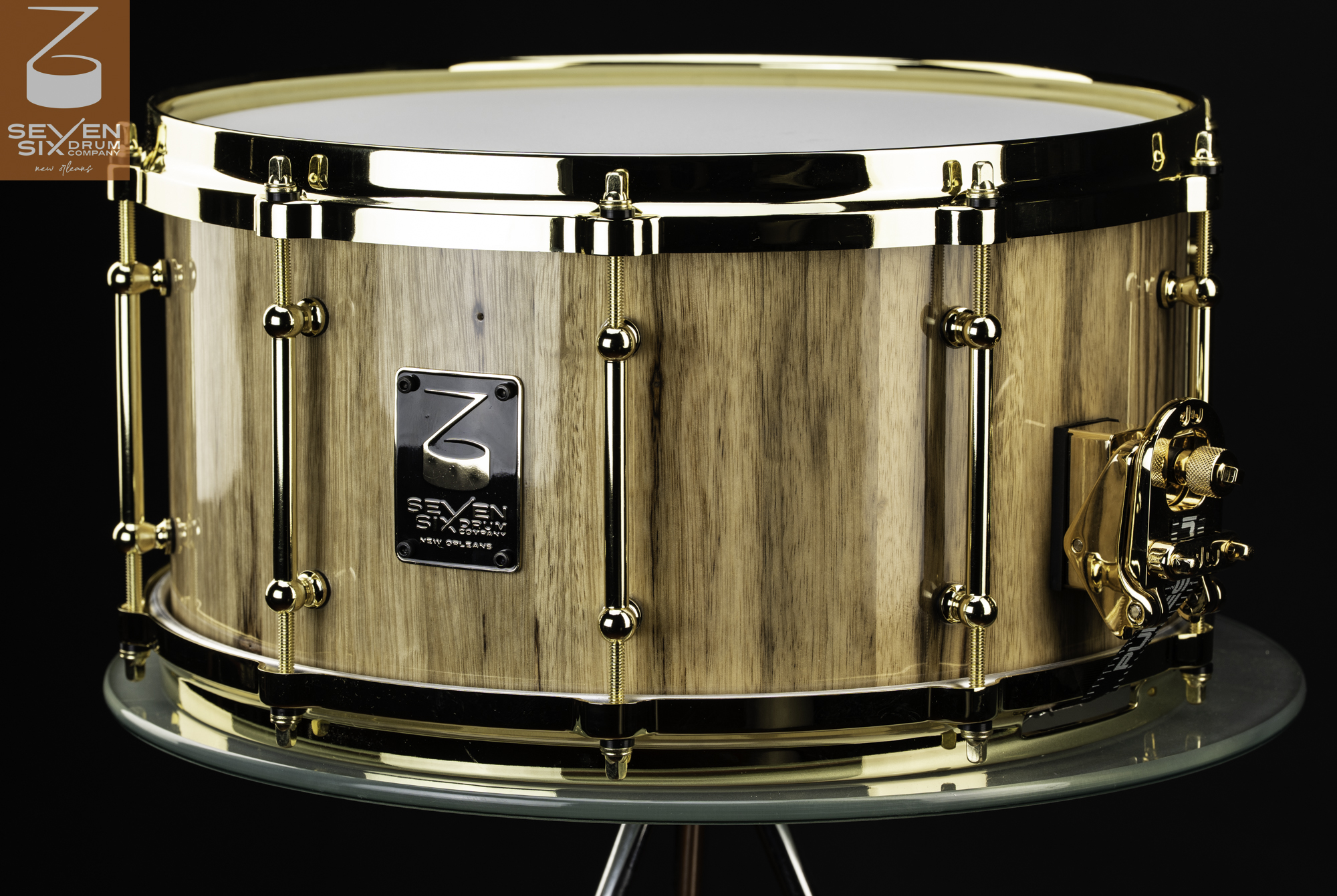 Handmade snare drum with a glossy natural wood shell, polished gold hoops, tube lugs, and throw-off.