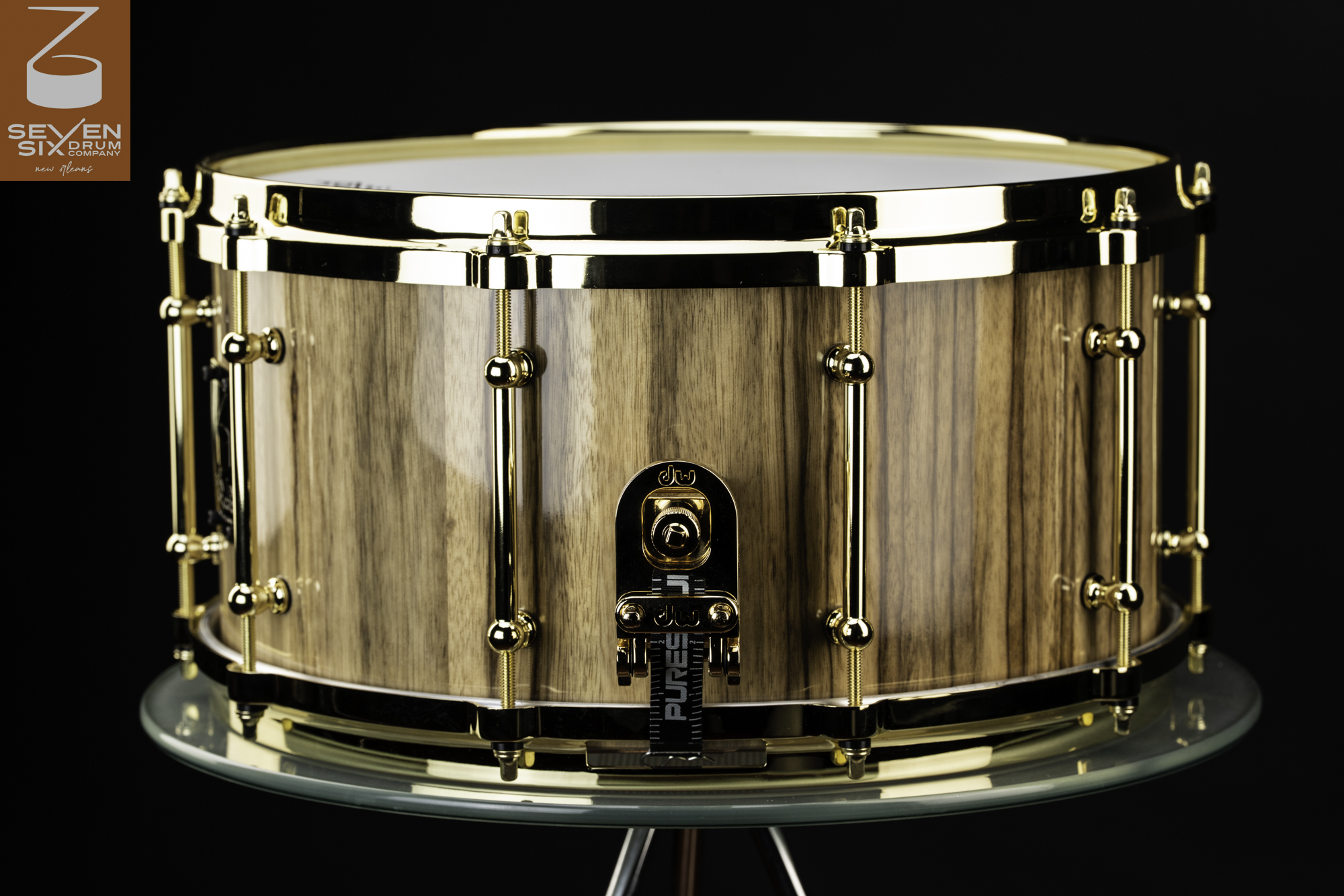 Handmade snare drum crafted from glossy natural wood with polished gold hoops, tube lugs, and throw-off hardware.