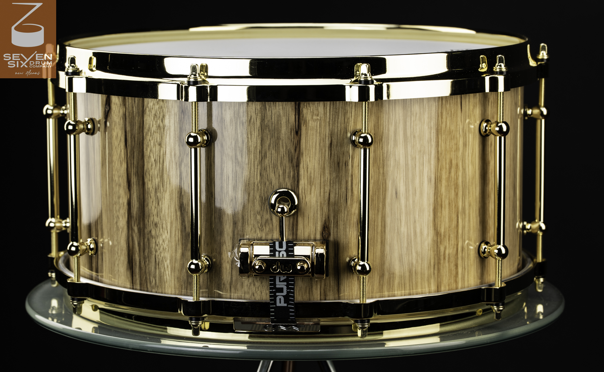 Handcrafted snare drum with a glossy natural wood grain shell, polished gold tube lugs, and matching gold hoops.