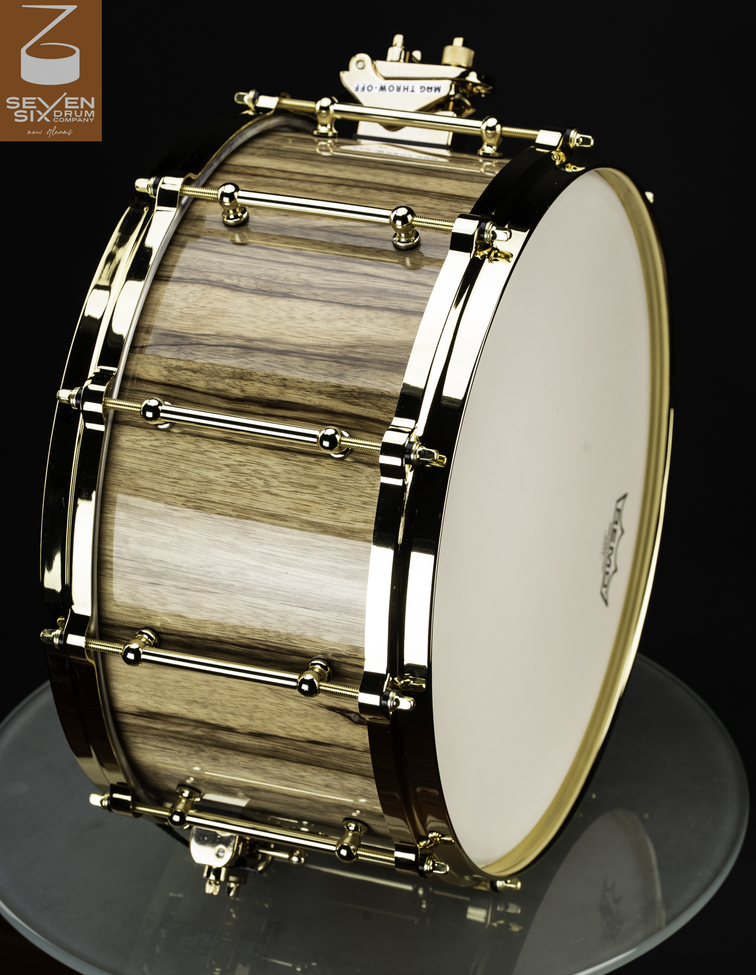 Handmade snare drum featuring a glossy natural wood shell with polished gold hoops and tube lugs.