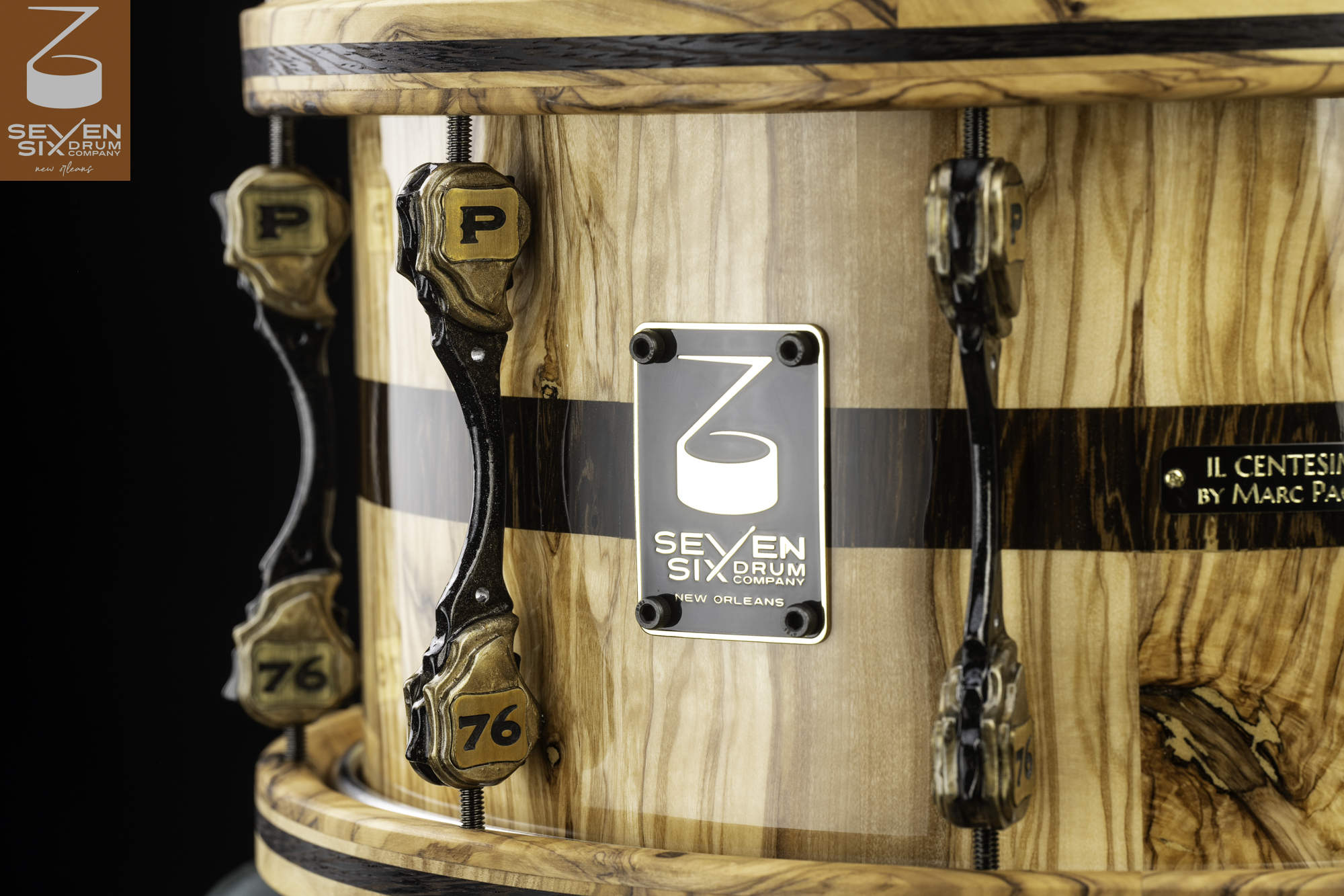 Glossy natural wood snare drum featuring a dark center stripe, sculpted black and gold lugs, and matching wooden hoops.
