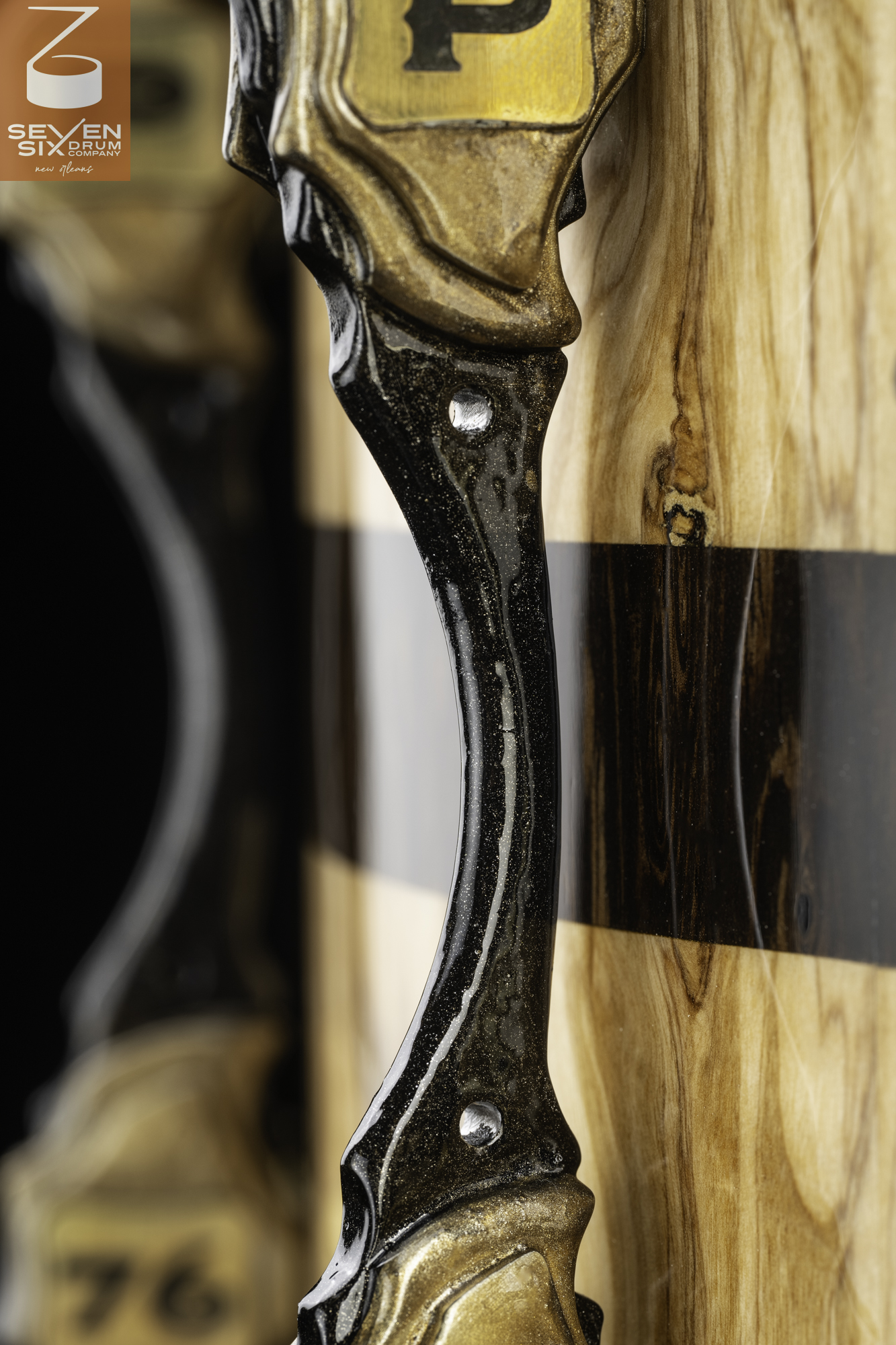 Glossy natural wood snare drum shell with a dark center stripe and a custom black and gold sparkle lug.