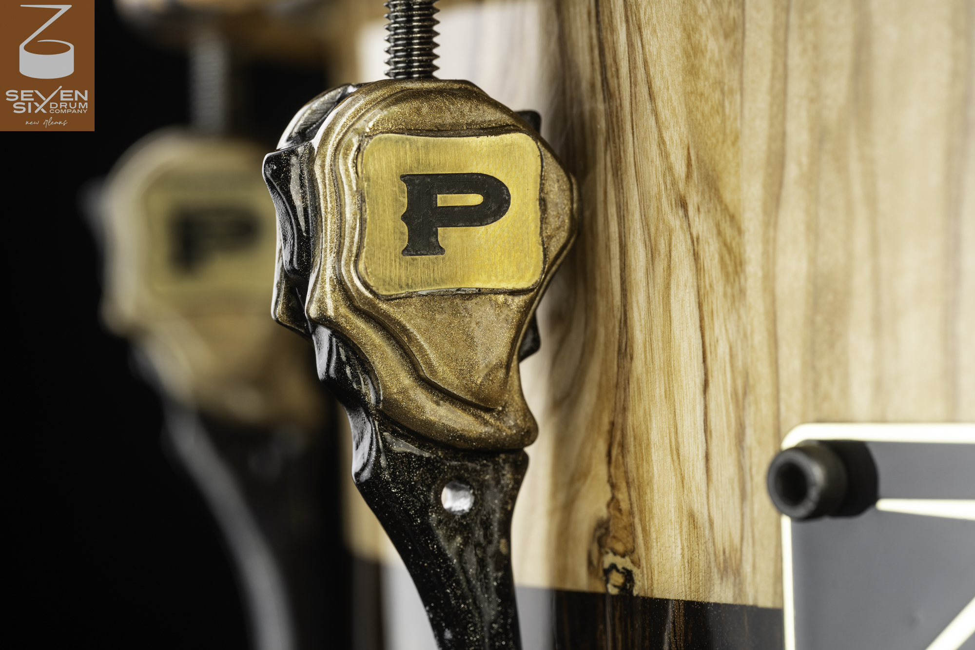 Natural wood snare drum with a satin finish, featuring a sculpted gold and black lug with a brass P badge.