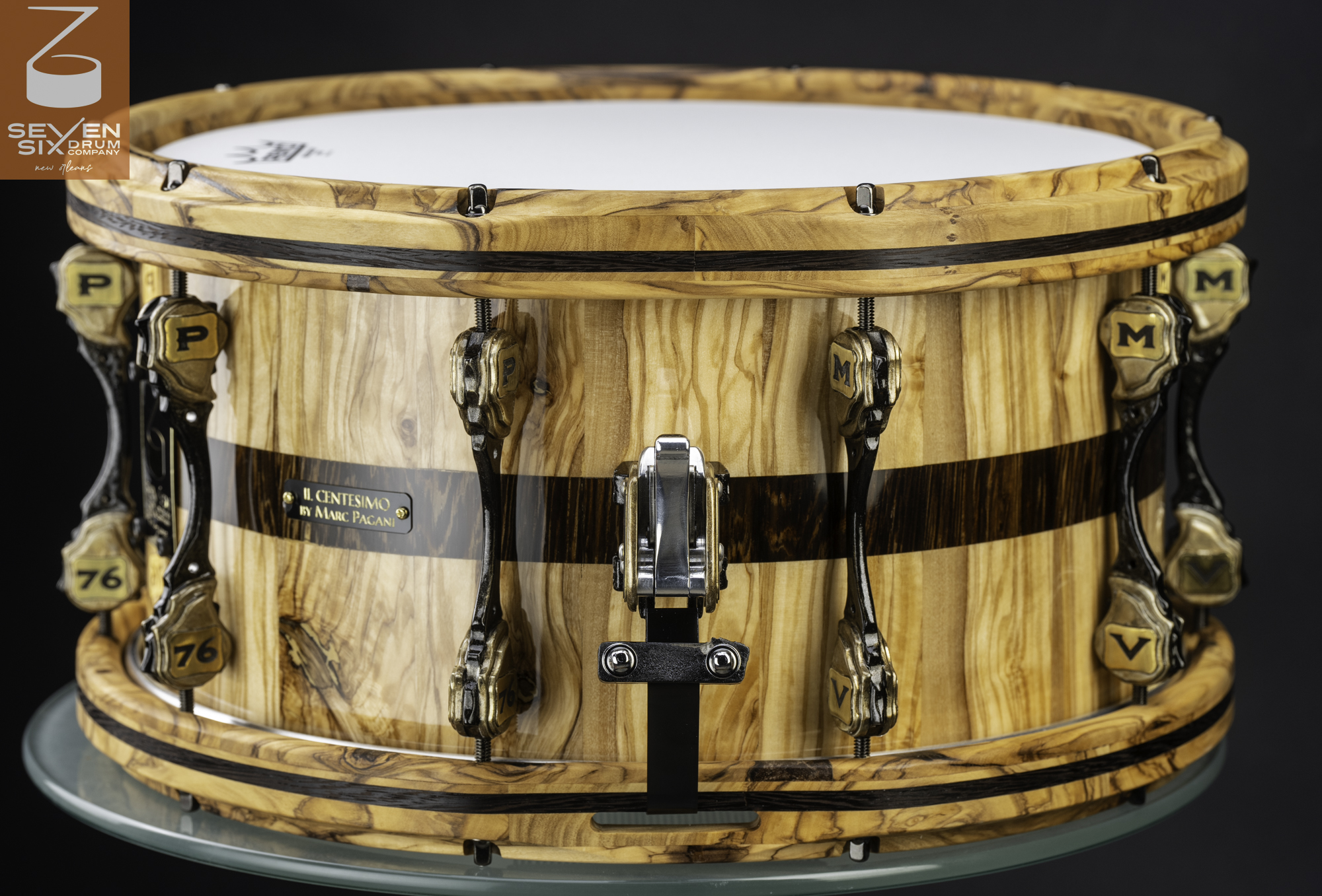 Handmade snare drum in gloss-finish wood with dark stripes, matching wood hoops, custom bronze lugs, and a chrome throw-off.