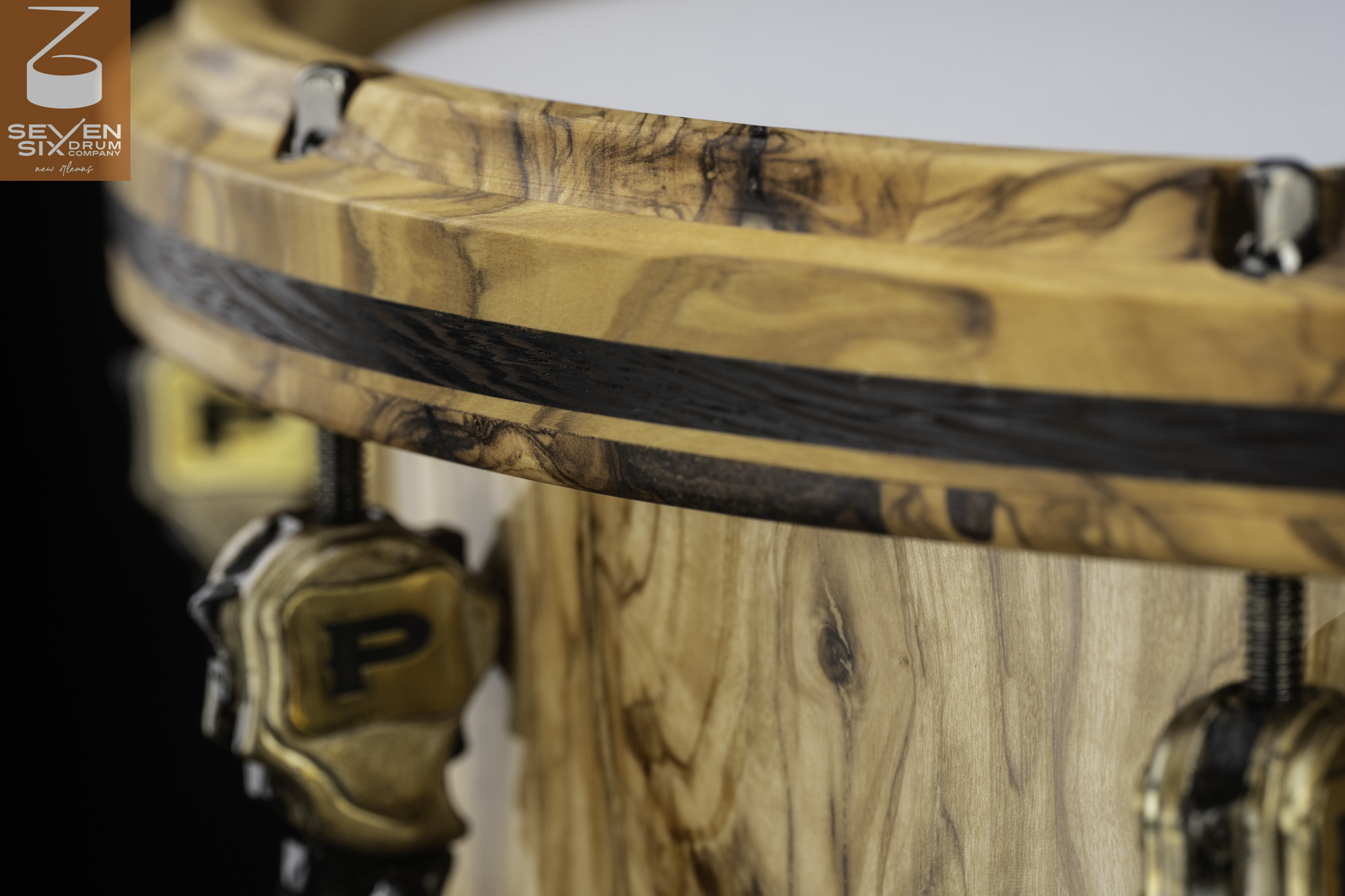 Handmade snare drum with a natural figured wood shell, dark-inlaid wooden hoop, and antique brass lugs.
