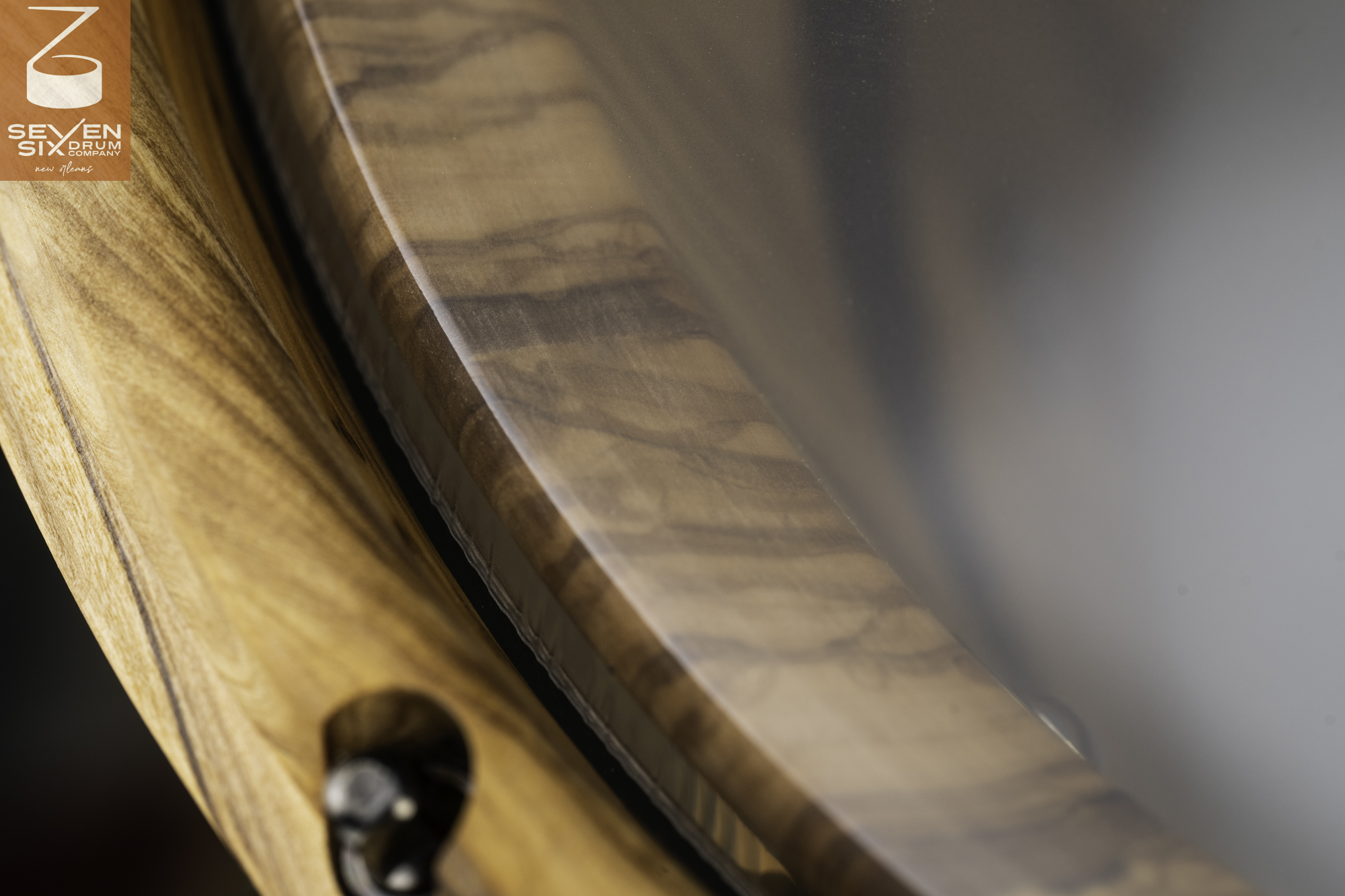 Natural wood snare drum hoop in a satin finish with a recessed tension bolt holding a clear drumhead to the shell.